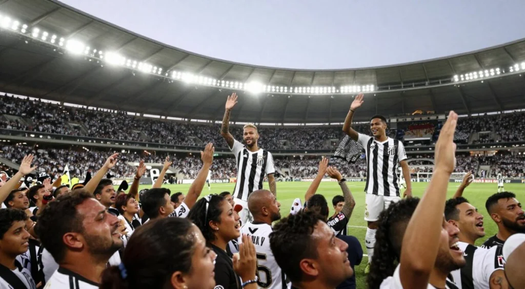 A vibrant farewell scene at the Vila Belmiro stadium, capturing the emotional moment of Neymar's departure from Santos FC. In the foreground, a crowd of fans, dressed in Santos jerseys, displays a mix of joy and nostalgia, with tearful eyes and raised hands, celebrating Neymar's legacy. The middle ground features Neymar in a respectful posture, wearing a club jersey, waving goodbye. Gabigol is positioned nearby, excited and ready for his debut, showcasing unity among players. Bright stadium lights illuminate the scene, casting a warm glow that contrasts with the evening sky. The atmosphere is filled with a sense of history and heartfelt emotion, reflecting the significant moment for both players and fans. The image is shot with a wide-angle lens, capturing the sweeping view of the stadium filled with supportive supporters.